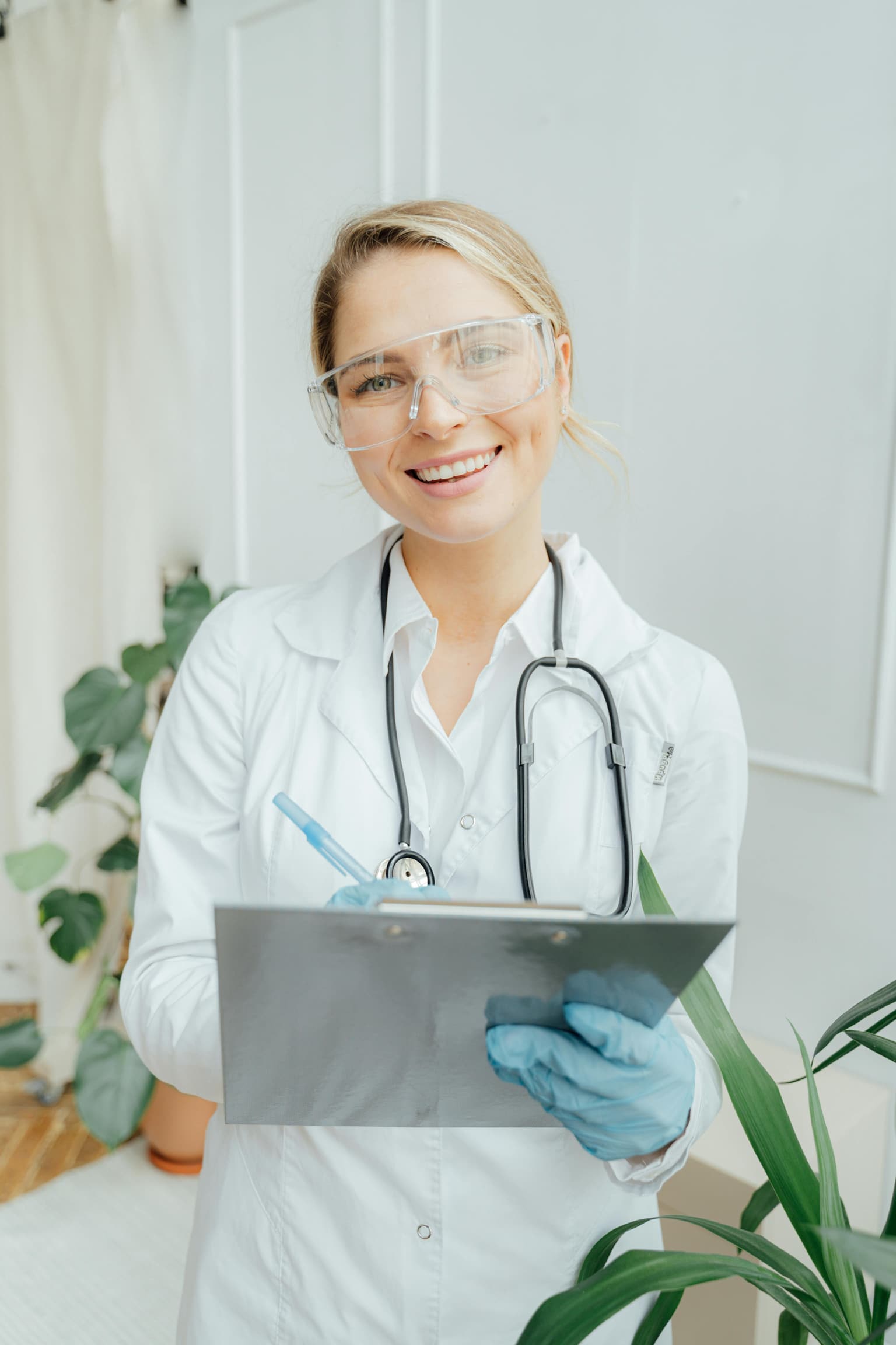 A smiling clinician in safety glasses holding a patient chart