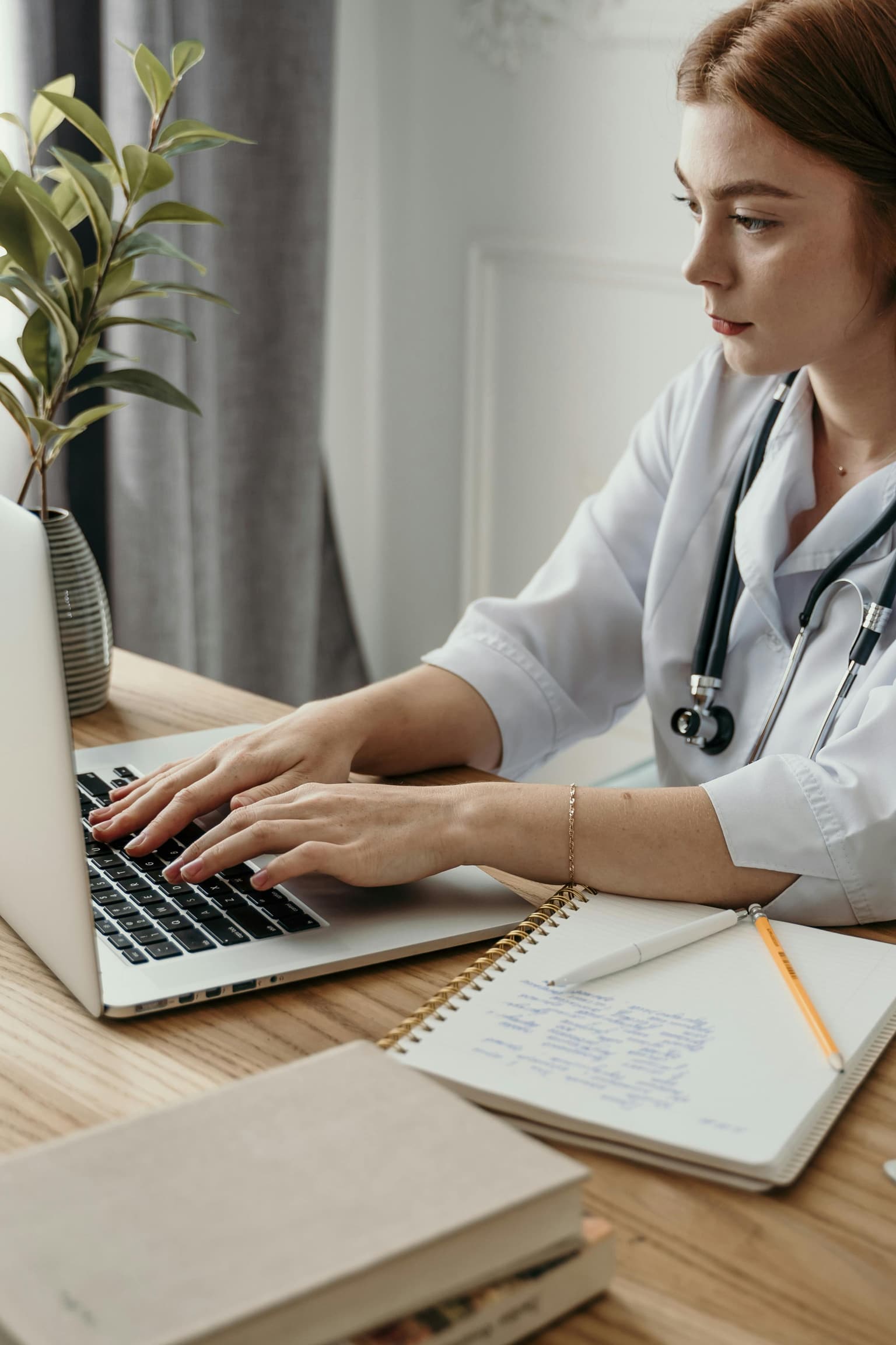 A doctor taking follow-up notes at a laptop during a remote consultation